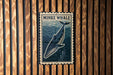 a metal sign with a picture of a whale, mounted on a wooden wall.