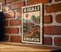 A vintage-style postage stamp featuring a cityscape and a sun in the sky, hanging on a brick wall.