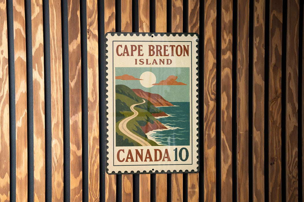 A vintage-style postage stamp from Cape Breton Island, Canada, featuring a scenic coastal landscape with a winding road and a full moon.