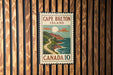 A vintage-style postage stamp from Cape Breton Island, Canada, featuring a scenic coastal landscape with a winding road and a full moon.