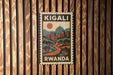 A vintage-style postage stamp from Rwanda featuring a cityscape and a sun in the sky.