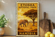 a decorative stamp or sign with an illustration of an elephant in a savanna landscape, surrounded by trees and mountains, with the text "ETOSHA NATIONAL PARK NAMibia" prominently displayed.