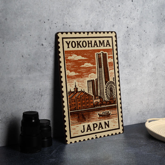 A metal stamp depicting a cityscape with a ferris wheel, buildings, and a river, with the text "Yokohama Japan" printed on it.