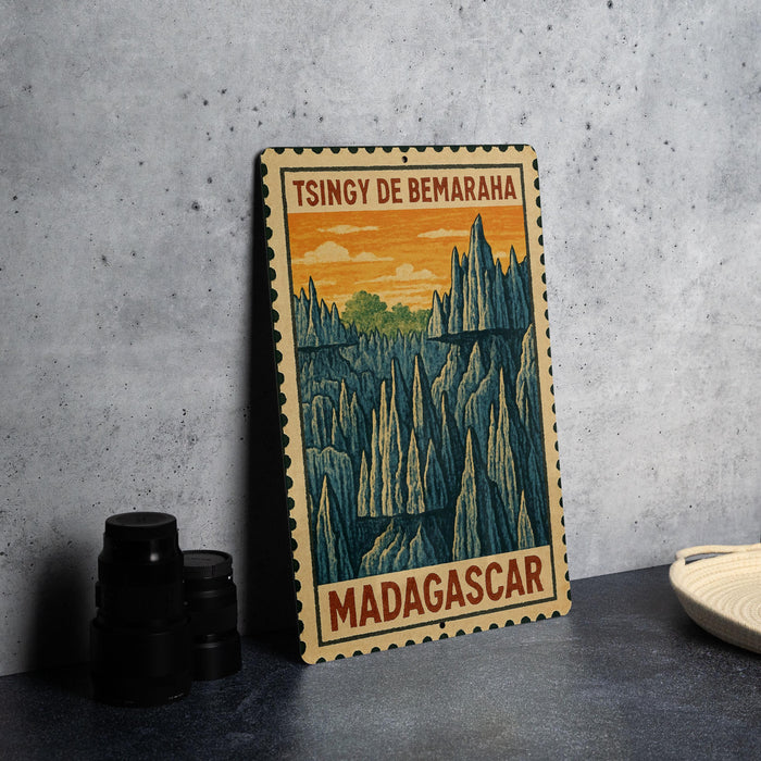 A vintage-style metal stamp depicting a mountainous landscape with the text "TSINGY DE BEMARAH" and "MADAGASCAR" printed on it, placed on a gray countertop next to some black camera lenses.