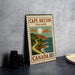 A vintage-style metal sign for Cape Breton Island, Canada, featuring a scenic illustration of a coastal landscape with mountains, a winding road, and a full moon.