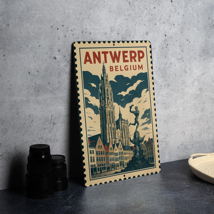 A vintage-style metal sign with the text "ANTWERP BELGIUM" and an illustration of a cityscape, including a church and a statue, is displayed on a gray concrete surface.