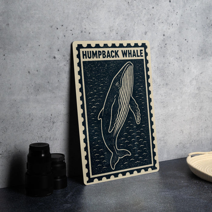 a framed artwork of a humpback whale, which is placed on a table next to some black camera lenses.
