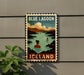 A vintage-style sign for Blue Lagoon, Iceland, featuring a woman swimming in a lake surrounded by mountains.