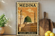 A vintage-style metal stamp depicting the Medina, the largest city in Saudi Arabia, with the text "SAUDI ARABIA" printed on it. The stamp is displayed on a shelf, surrounded by various kitchen items such as a wooden cutting board, a lemon, and a potted plant.