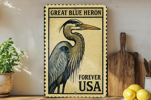A vintage-style postage stamp featuring a great blue heron, with the text "GREAT BLUE HERON FOREVER USA" printed on it. The stamp is displayed on a shelf next to a wooden cutting board and a potted plant.