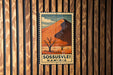 A vintage postage stamp depicting a desert landscape with a mountain in the background, hanging on a wooden wall.