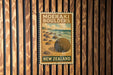 A vintage-style poster for Moeraki Bowlers, a famous rock formation in New Zealand, is displayed on a wooden wall.