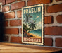 A vintage-style poster of a tropical beach scene with palm trees and a blue sky, hanging on a brick wall.
