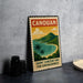 A vintage-style metal sign with a tropical island landscape and text, placed on a gray countertop next to some black camera lenses.