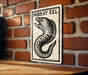 A metal sign with a black and white illustration of a fish, mounted on a brick wall.