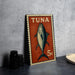 a Tuna stamp with a fish illustration, placed on a table next to some black camera lenses.