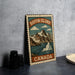 A metal sign with a mountain landscape and the text "Baffin Island Canada" is displayed on a table.