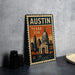 A vintage-style metal sign with the text "AUSTIN TEXAS USA" and an illustration of the Texas State Capitol building, placed on a gray countertop next to some black camera lenses.