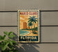A vintage-style metal sign with a tropical beach scene and palm trees, mounted on a wall.