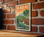 A vintage-style metal sign with the text "HAWAII, USA" and an illustration of a mountainous landscape with a waterfall.