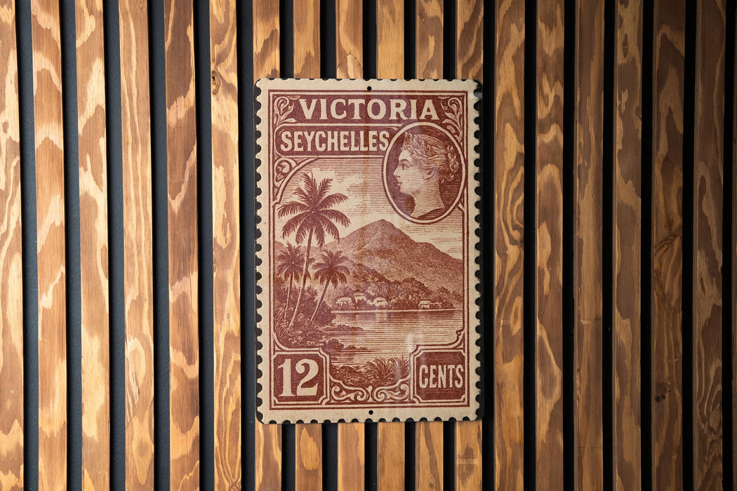 A vintage postage stamp from Victoria Seychelles, featuring a tropical landscape with palm trees and a mountain in the background.