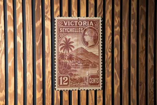 A vintage postage stamp from Victoria Seychelles, featuring a tropical landscape with palm trees and a mountain in the background.