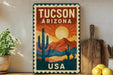 A vintage-style metal sign displaying the text "Tucson, Arizona USA" with a desert landscape and cacti illustration.