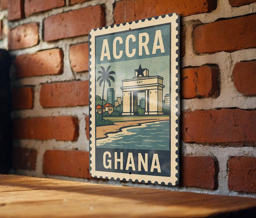 A vintage-style metal sign with the text "ACCRA GHANA" is displayed on a brick wall, featuring an illustration of a cityscape and a palm tree.