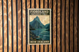 A vintage-style postage stamp depicting a scenic landscape with mountains, water, and a wooden fence in the background.