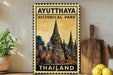 a vintage-style stamp or sign with the text "AYUTTHAYA HISTORICAL PARK THAILAND" and an illustration of a temple or pagoda. The sign is displayed on a shelf, with a potted plant to the left and a wooden cutting board to the right.