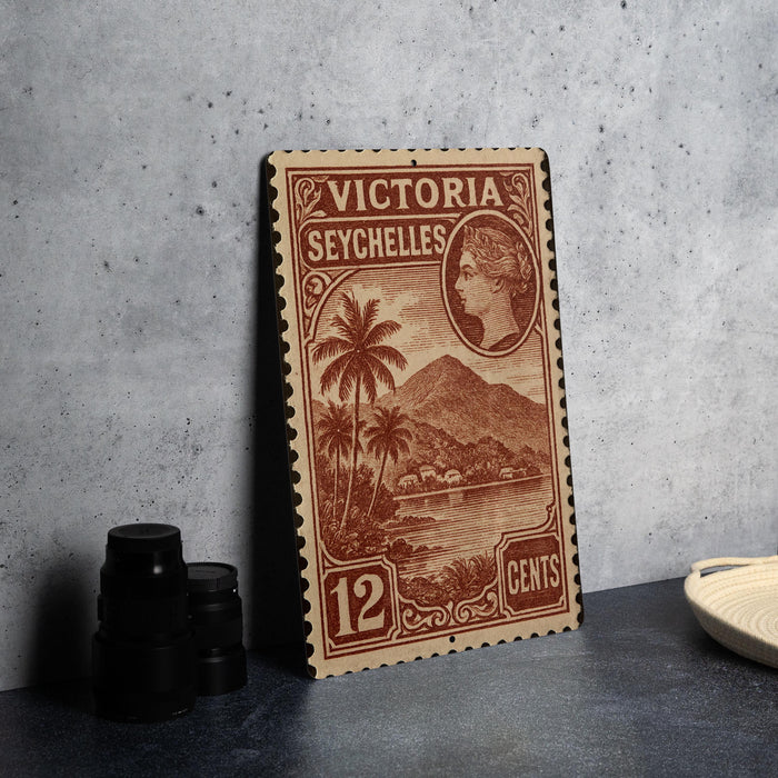 A vintage postage stamp from Victoria Seychelles, featuring a tropical landscape with palm trees and mountains, is displayed on a table.