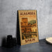 A metal sign with a vintage-style illustration of a castle and a pool, labeled "ALHAMBRA" and "SPAIN", is displayed on a table.