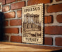A wooden sign with an illustration of an ancient building, mounted on a brick wall.