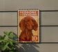 A vintage-style stamp featuring a redbone coonhound dog, mounted on a wall next to a plant.