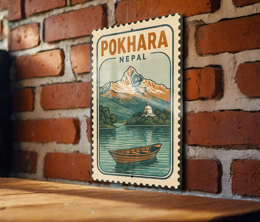 A vintage-style postage stamp depicting a scenic mountain landscape with a small boat on a lake, hanging on a brick wall.