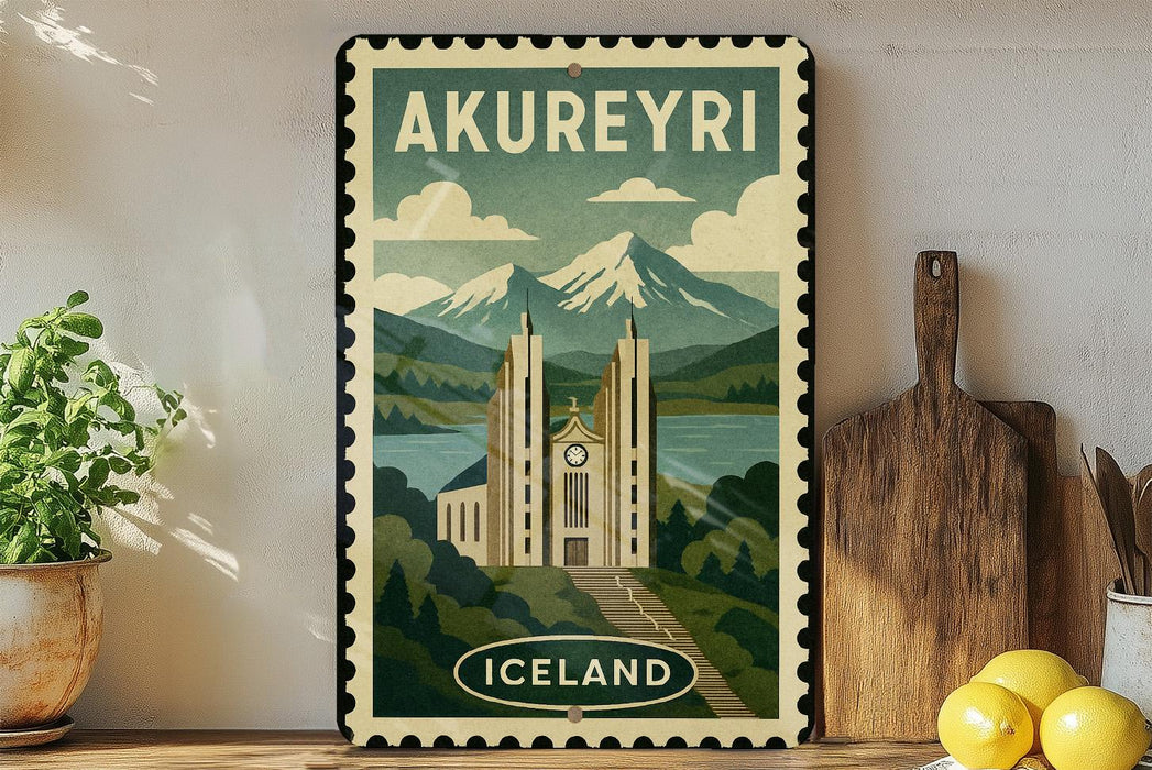 A vintage-style metal sign with the text "AKUREYRI" and an illustration of a castle or cathedral, surrounded by mountains and a lake, is displayed on a shelf with a potted plant, a wooden cutting board, and some lemons.