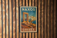 A vintage-style postage stamp from Greece featuring a coastal city with a temple or monument in the background.