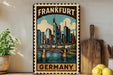 A framed vintage-style poster of the city of Frankfurt, Germany, featuring a bridge and skyline, is displayed on a wall next to a wooden cutting board and some potted plants.