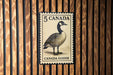 A 5 Canada goose postage stamp is displayed on a wooden wall.
