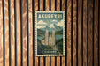 A vintage-style poster of Akureyri, the capital city of Iceland, is displayed on a wooden wall.