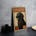 A flat-coated retriever dog illustration on a postage stamp-like sign, placed on a countertop next to some black camera lenses.