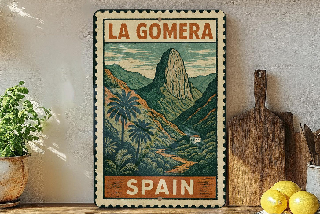 A vintage-style metal sign with a mountain landscape and palm trees, featuring the text "LA GOMERA" and "SPAIN" on it, is displayed on a shelf next to a wooden cutting board and some potted plants.