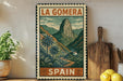 A vintage-style metal sign with a mountain landscape and palm trees, featuring the text "LA GOMERA" and "SPAIN" on it, is displayed on a shelf next to a wooden cutting board and some potted plants.