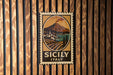 A vintage-style metal sign with a landscape and a mountain, mounted on a wooden wall.