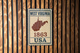 A vintage-style metal sign with the text "WEST VIRGINIA 1863 USA" displayed on a wooden wall.