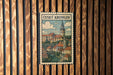 A vintage-style poster depicting a town with a church and a castle, hanging on a wooden wall.