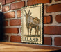 a wooden table with a framed illustration of a horned animal, likely a gazelle or similar species, mounted on a brick wall.