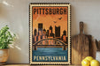 A vintage-style metal sign depicting the Pittsburgh skyline with a bridge, placed on a wooden surface next to a wooden cutting board and some lemons.