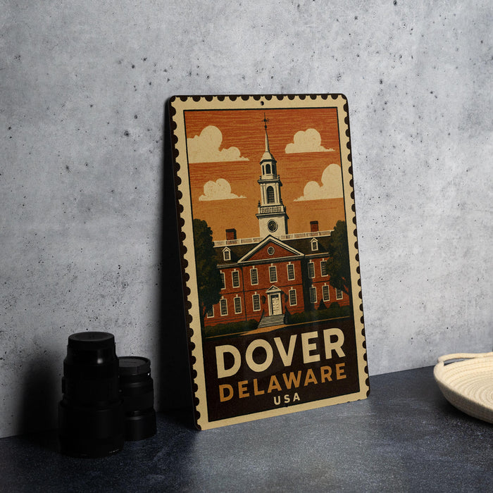 A metal sign with an illustration of a building and a church, along with the text "Dover, Delaware USA" on it, is displayed on a table.