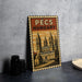A vintage-style metal sign with a castle illustration and the text "PÉCS HUNGARY" (Pécs Hungary) on it, placed on a gray surface next to some black camera lenses.